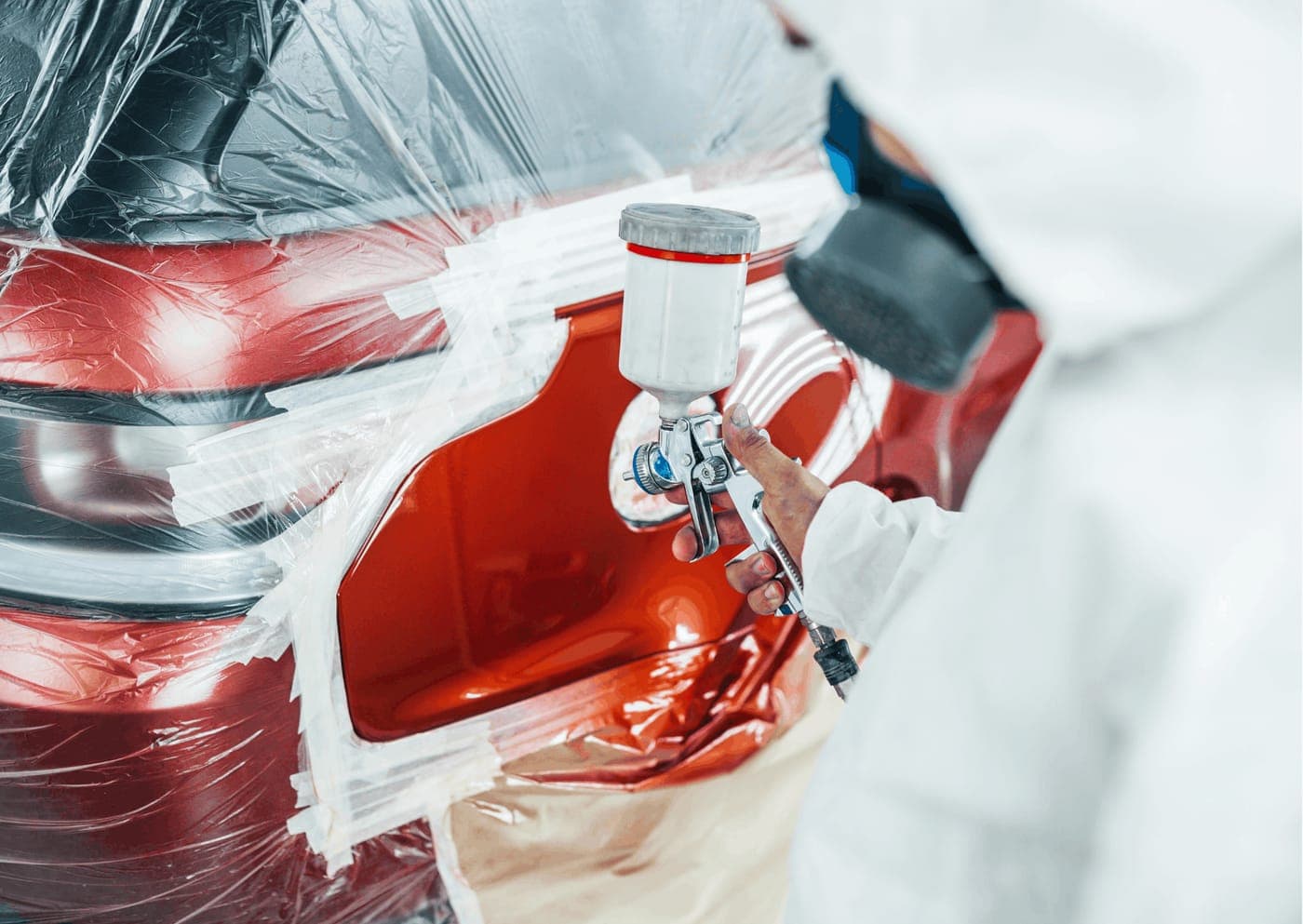 Panel beater spray painting a repaired rear quarter panel on a masked vehicle